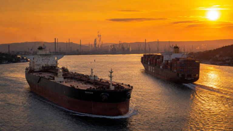 Container ship and oil tanker navigating a strait at dawn with refinery silhouette and orange sunrise